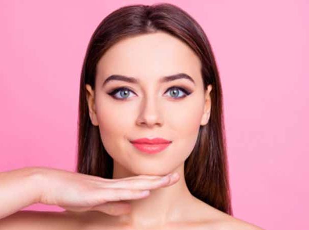 Woman with long brown hair in front of a pink background